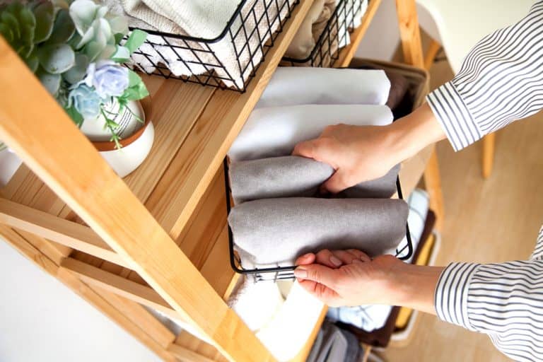 Spring cleaning of closet. Vertical tidying up storage. Neatly folded bed sheets in the metal black baskets for wardrobe. Nordic style.